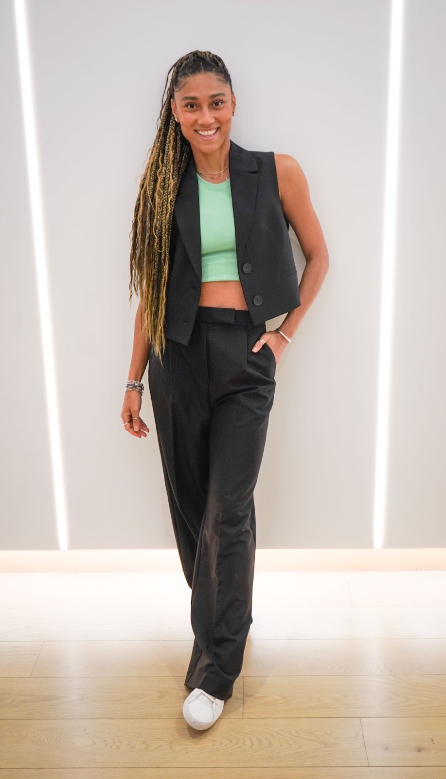 A woman smiling at camera wearing a mint green tank top with suit pants and an open suit vest.