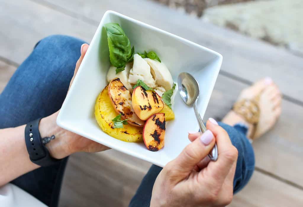 A bowl of grilled peaches and pineapple with ice cream and basil