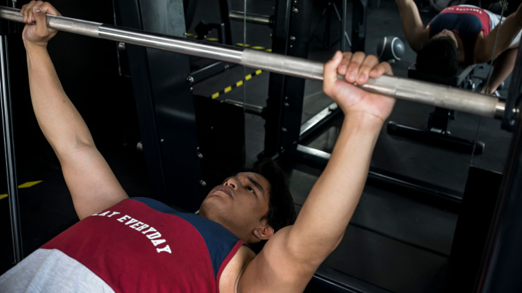 A person using a Smith Machine to bench press.