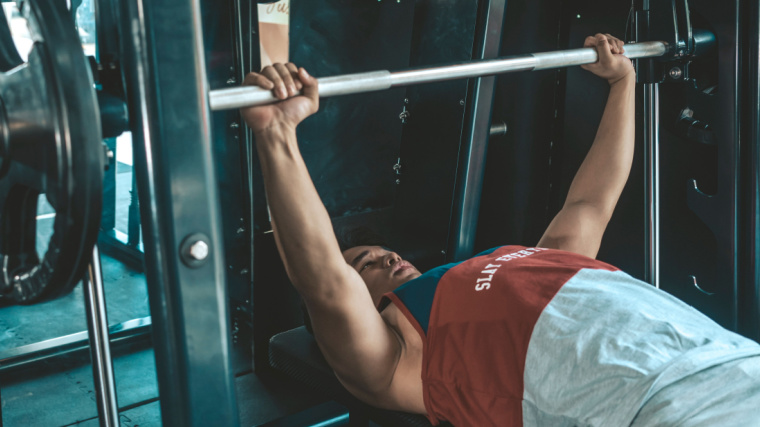 A person gripping the barbell during a Smith machine bench press.