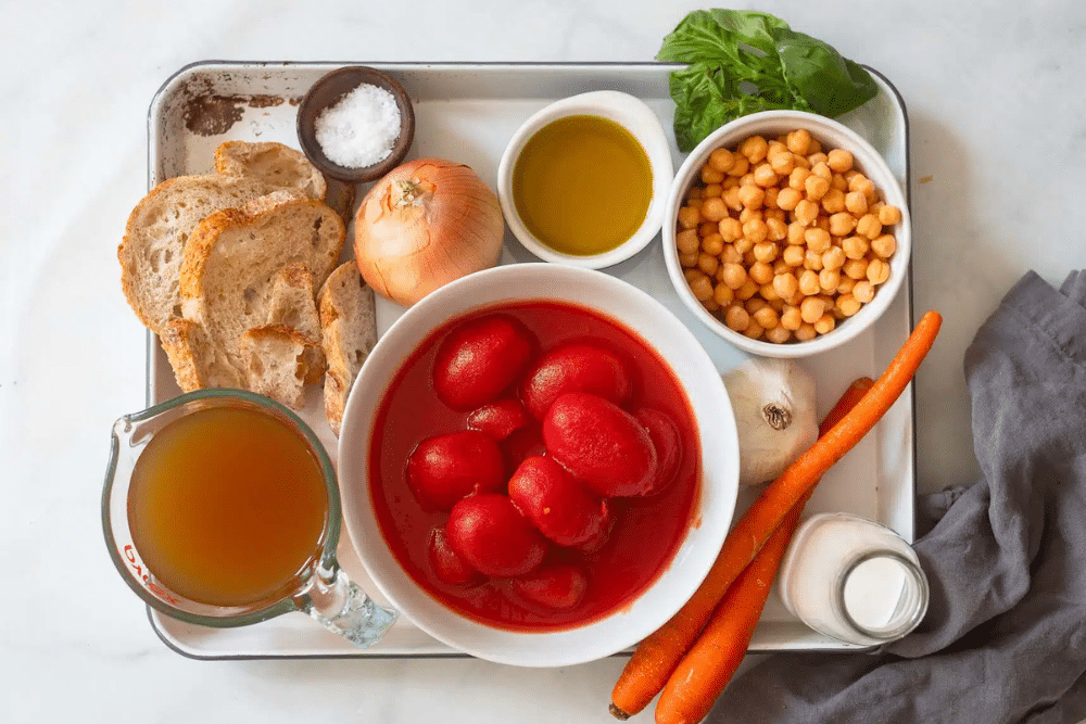 The ingredients of Tuscan soup, including whole tomatoes, onion, basil, carrots, and garbanzo beans.