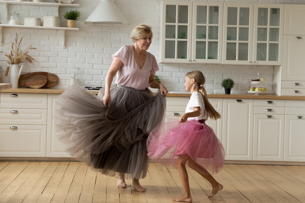 A grandmother dancing in the kitchen with her granddaughter.