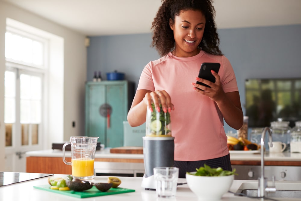 A woman in a pink shirt blending a smoothie in the kitchen.