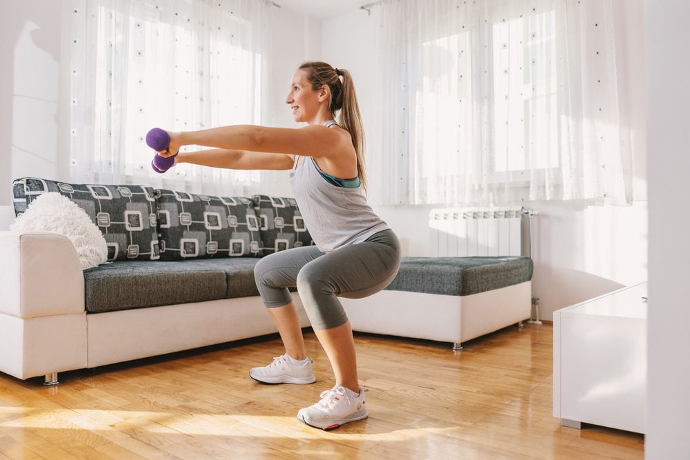 A woman holding dumbbells while doing squats in her living room.