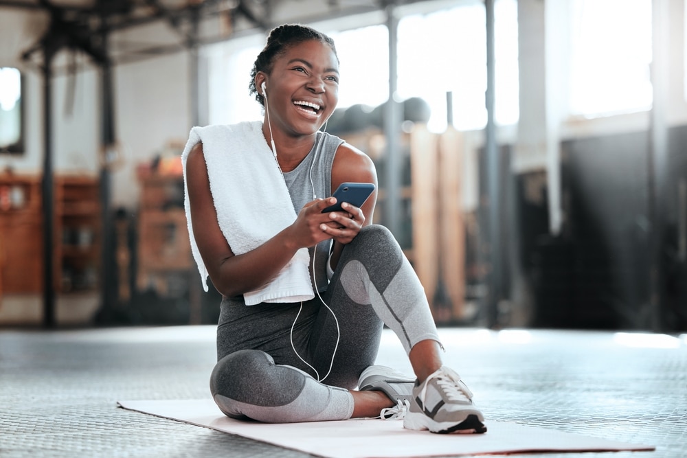 A woman laughing at her phone while taking a break from exercising at the gym.