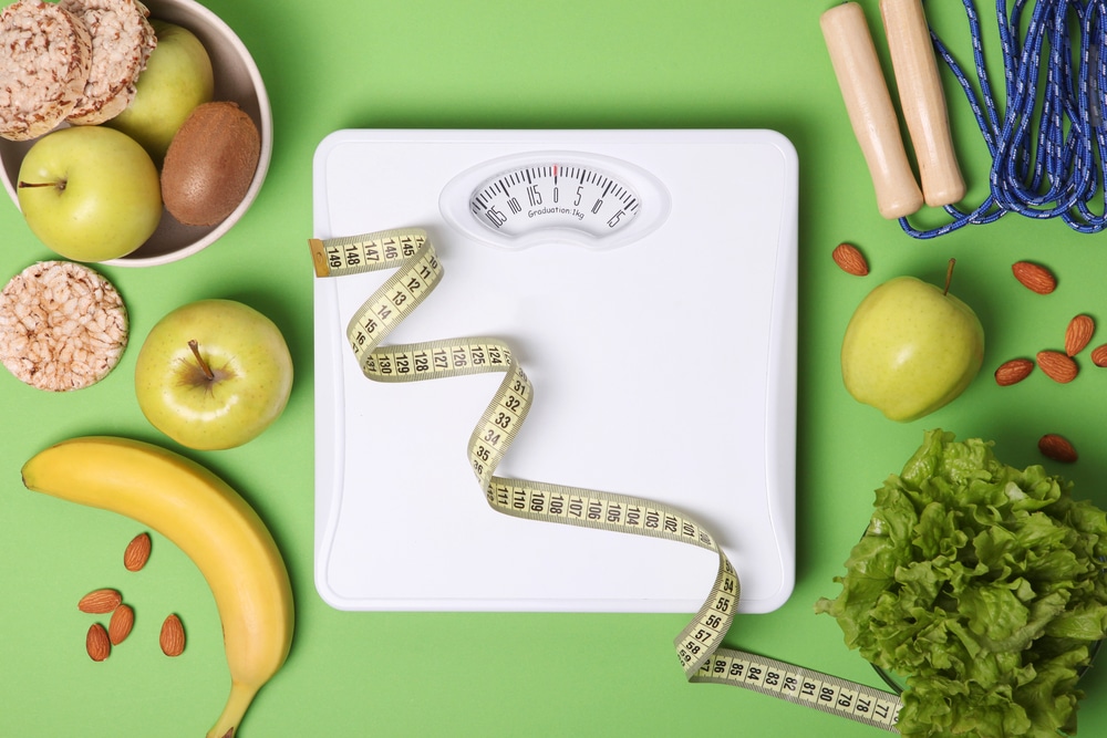 A floor scale and tape measure surrounded by healthy foods on a green background.