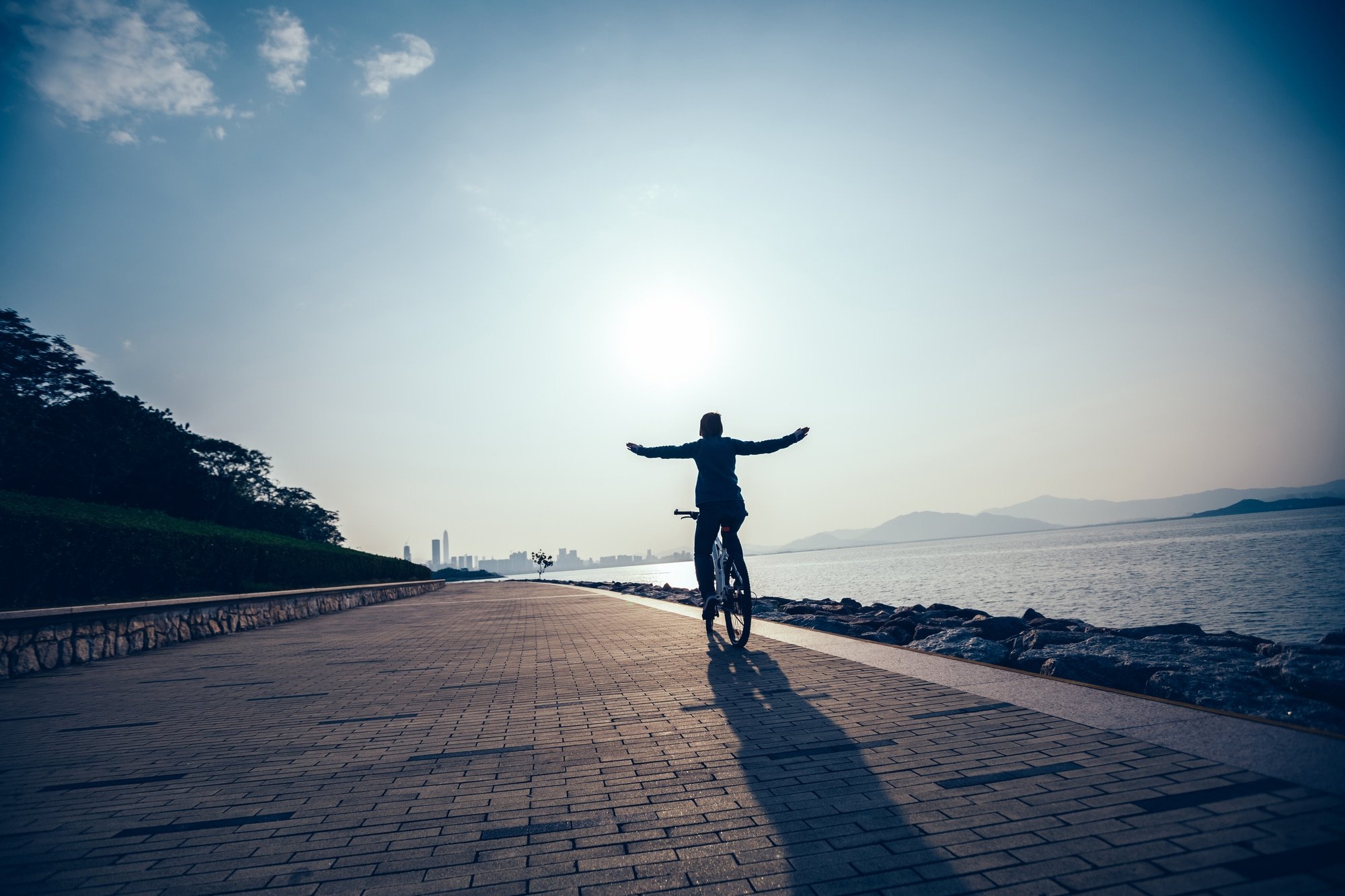 Silhouette of a cyclist riding a bike in the sunrise by the water.