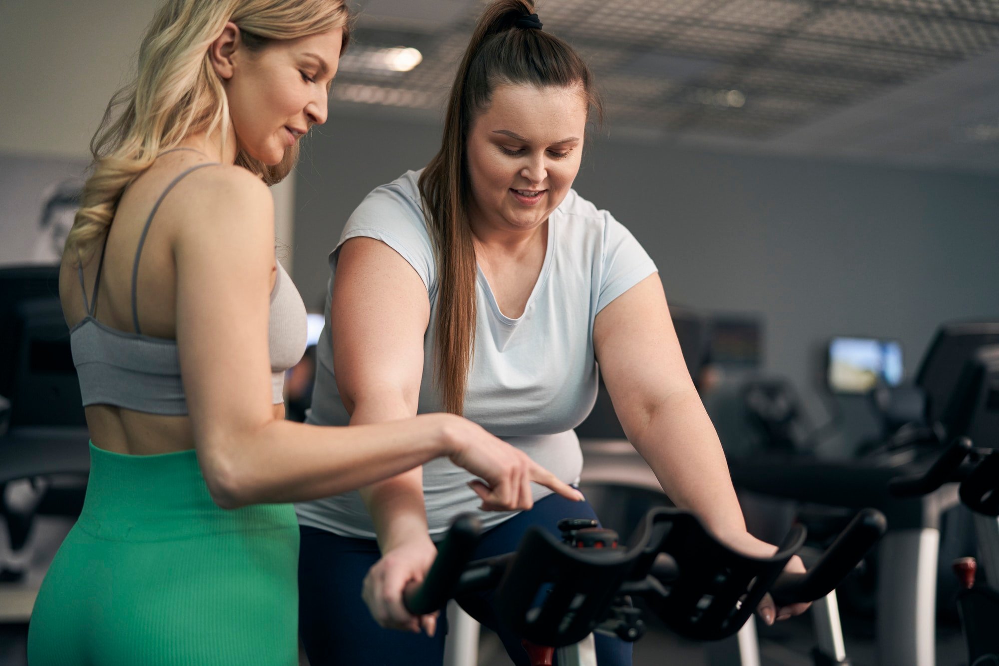 Instructor helping plus size woman on a stationary bike at the gym.