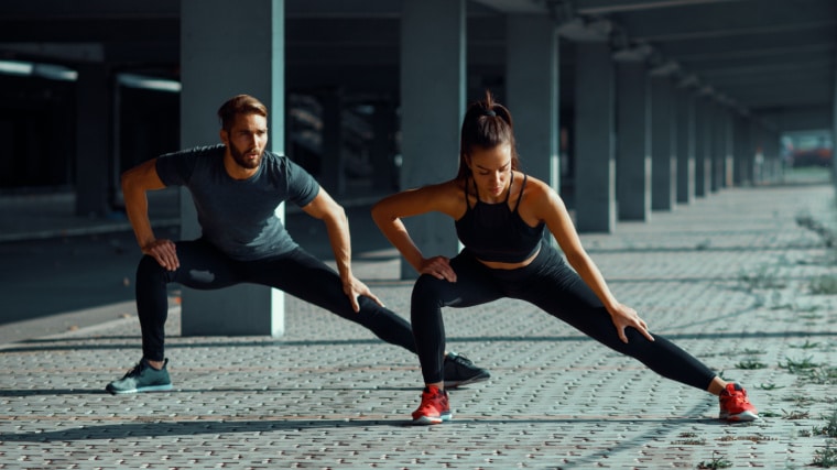 Two fit individuals stretching their legs outdoors.